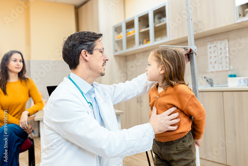 Quadro su tela Male pediatrician checking the height and weight of a small child in the clinic