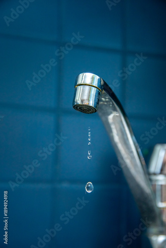 Leaking faucet drips water against blue tiled wall