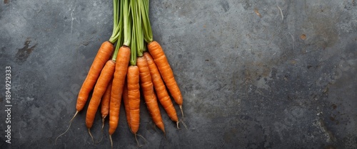 Fresh carrots arranged in bunch on grey stone surface from above