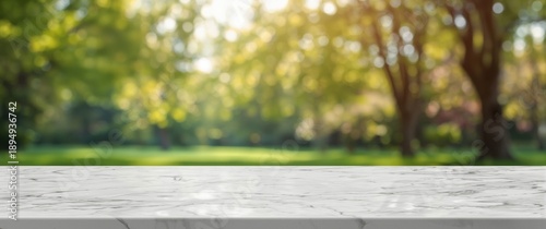 Empty white marble table surface with a blurred park tree and bokeh lights in background, display template for your design, advertising banner for products, panoramic perspective