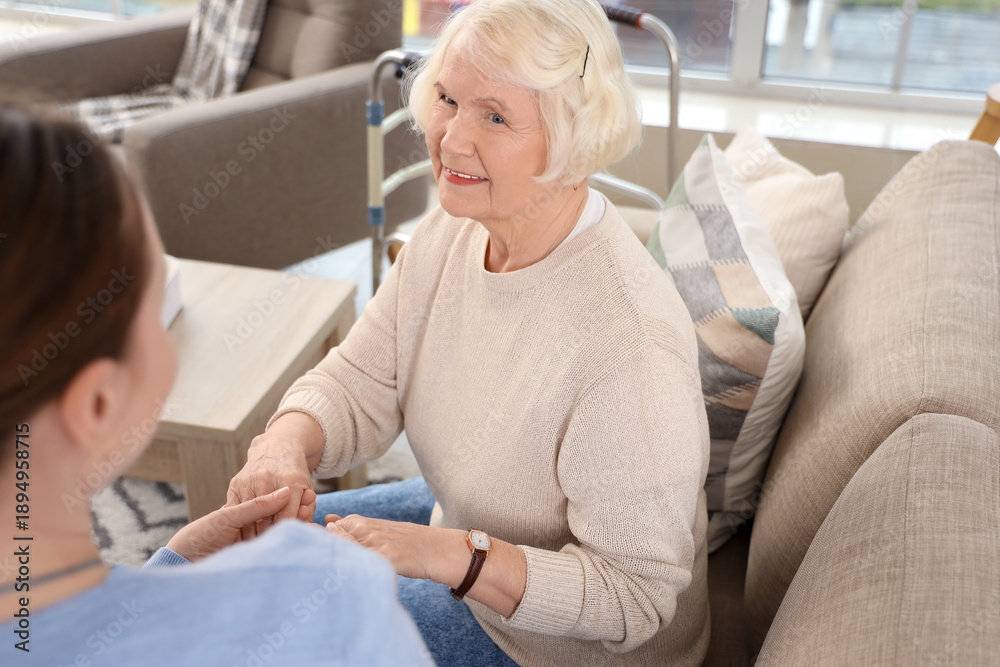 Fototapeta premium Caregiver and senior woman sitting on sofa in nursing home