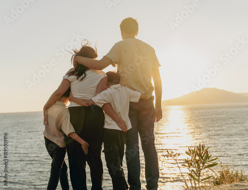Fotografie Young family with two sons hugging and watching sunset at the sea, travel and to