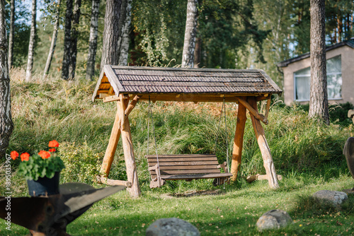 Photos Wooden swing set with a thatched roof in a lush green garden surrounded by trees