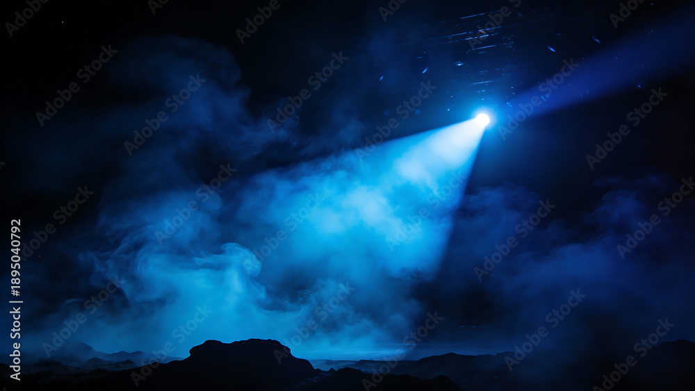 Fototapeta premium A dramatic blue spotlight cuts through thick, atmospheric smoke and fog on a dark, desolate landscape, creating a mysterious and theatrical effect.