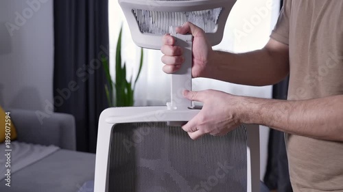 Man installing adjustable headrest on mesh ergonomic office chair. Close up of furniture assembly at home, modern workspace, unbranded office furniture.