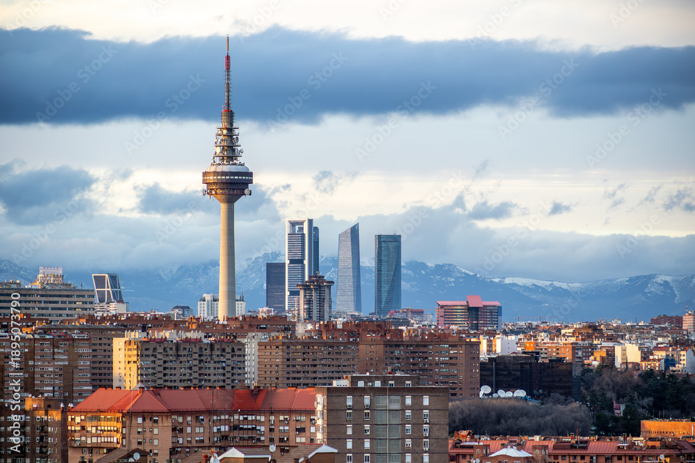 Obraz premium Urban landscape of Madrid with TV tower, residential roofs, green winter trees and modern skyline on the horizon.