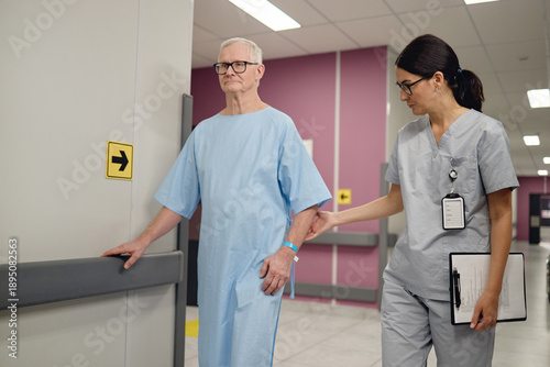 Valokuva Senior Caucasian man walking in hospital corridor with assistance from young adu