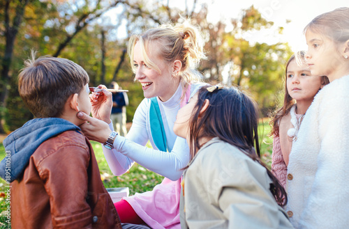 Obraz na płótnie Female animator painting a child's face with a brush at an outdoor birthday party in a park