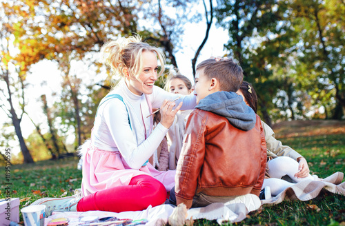 Fotografie Female animator painting a child's face with a brush at an outdoor birthday party in a park