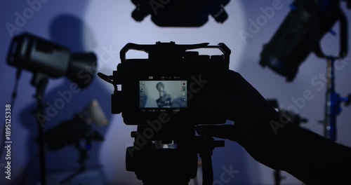The operator turns on and adjusts the camera in a photo studio with lighting equipment. A mannequin is displayed on the camera screen. Backstage photo shoot with professional lighting equipment.