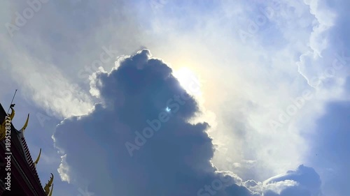 The Sun's Shining Behind Big Cloud and Bird on Part of Roof of Temple on Blue Sky Background with Bird Flying Compound of a Monastery at Bangkok, Thailand. 19 MAY 2025, A.M./ Slow Down Video