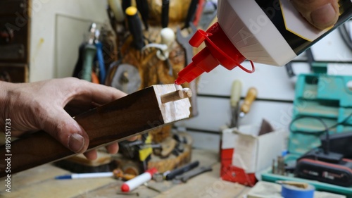 The carpenter's hands are holding a wooden object with wooden connecting fasteners inserted into the holes on the cut surface, and a bottle of glue, which is being applied to the fasteners for joining