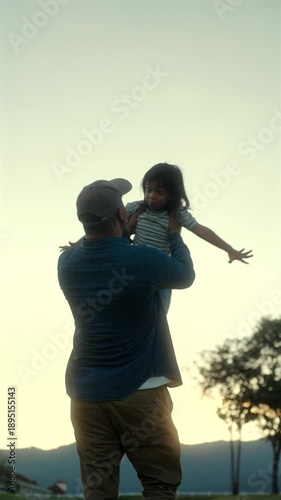 Vertical of father carrying his son and spinning around playful family bonding during sunset at the park, parent care with joyful outdoor lifestyle, fatherhood and Father’s Day celebration concept.
