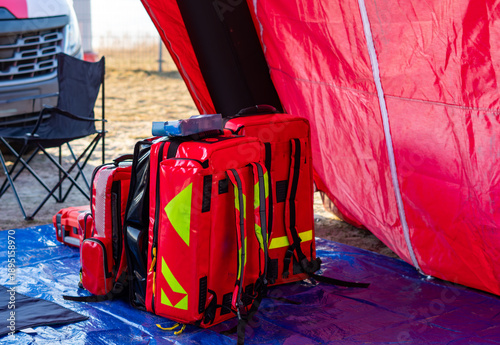 Red medical backpacks and emergency bags with reflective elements placed on a blue tarp in front of a red operational tent during rescue drills.