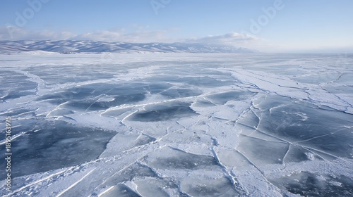 Expansive frozen lake surface with intricate cracks and snow-covered hills in the distance.