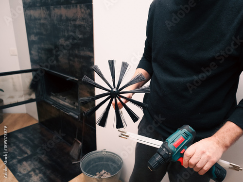 Man preparing to clean a modern indoor fireplace with a professional chimney brush.