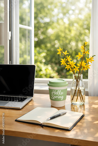 Home office by open window on Spring Equinox. Desk with laptop, vase of forsythia, 