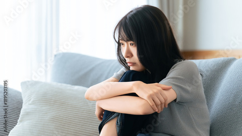 Photos ソファで落ち込んで座る女性の悩みイメージ, Depressed woman sitting alone on a sofa at home