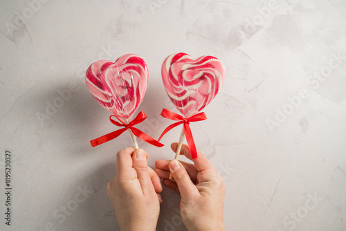 Valentine's Day festive background. Female hand holding heart-shaped lollipops on grey background with copy space. Love concept