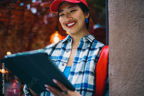 Fotografie Freelancer woman smiles while working on tablet outdoors, blending casual street fashion with digital focus and professional enthusiasm in mobile-connected freelance lifestyle