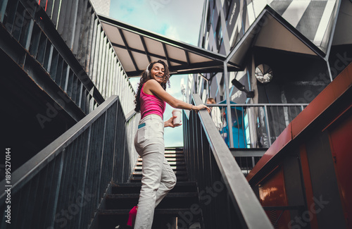 Photos Woman in headphones walks up stairs, turning with smile, holding coffee