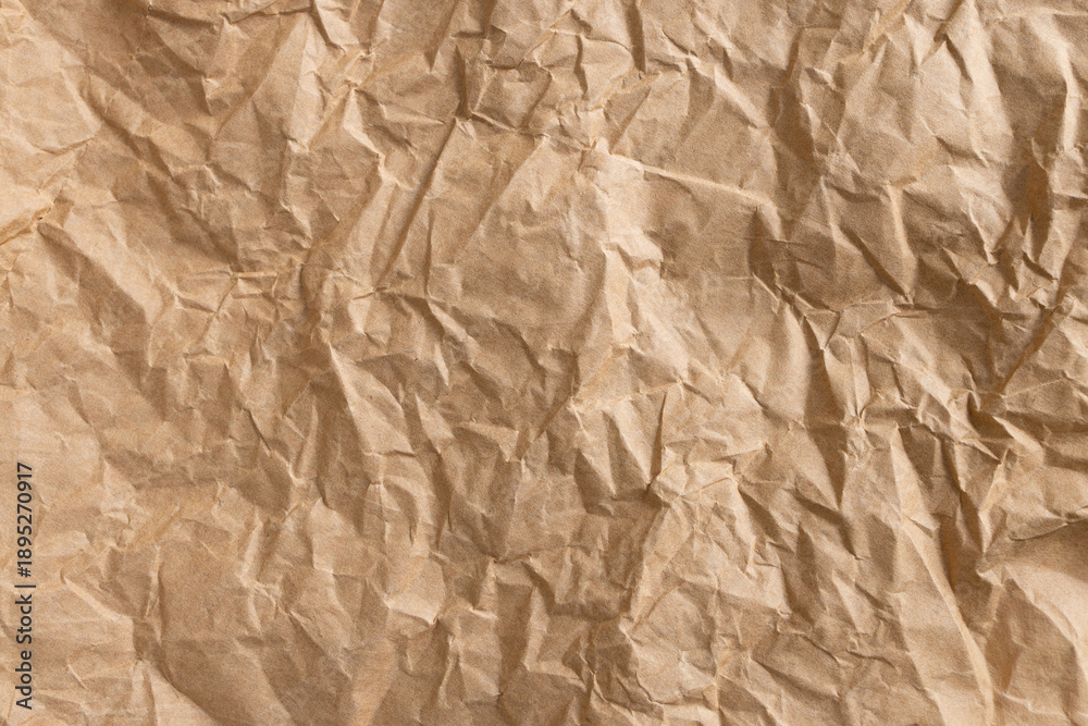 Fototapeta premium Crumpled brown kraft paper background macro,High-angle view of a sheet of crumpled brown kraft paper with heavy creases and wrinkled texture. This vintage-style aesthetic background is perfect.