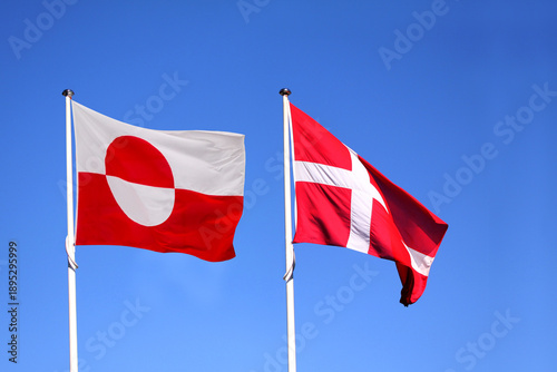 Greenland and Denmark - Greenlandic and danish national flags  waving side by side in the wind with blue sky on a sunny day as background