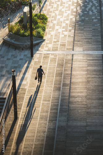 View of a lone figure walking along a geometrically patterned walkway, bathed in the warm glow of the late afternoon sun, Punggol, Singapore.