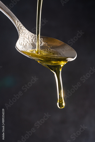 Organic olive oil pouring from spoon into glass bowl on black background	
