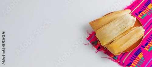 Wallpaper Mural Angled view of several tamales wrapped in natural leaves on a clay plate and traditional pink tablecloth with embroidery. Torontodigital.ca