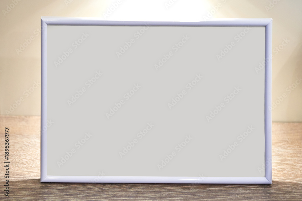 Fototapeta premium Blank white photo frame on wooden surface with soft lighting in simple neutral setting.