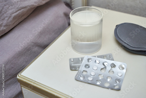 Photos Empty pill blisters, glass, and sleep mask on nightstand in calm bedroom setting, reflecting health and relaxation