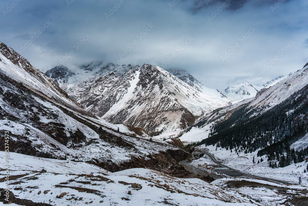 Obraz premium Scenic snowy valley with mountain pass, curving road, and winter landscape surrounded by steep slope