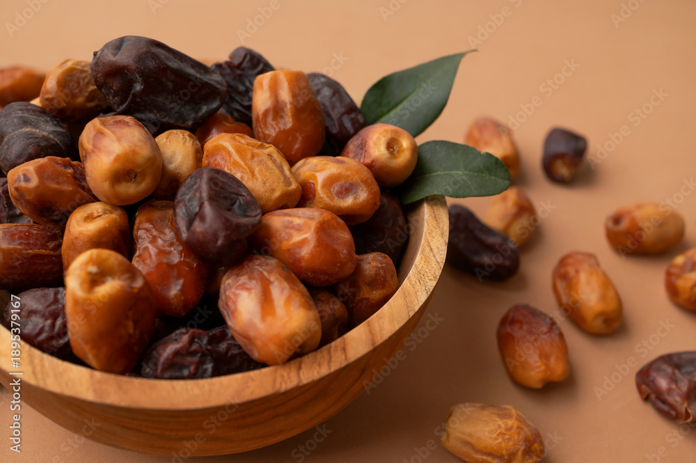 Obraz premium Dried dates in wooden bowl on brown background. Delicious sweet dried fruits flat lay top view. Date palm fruits, organic dates. Healthy vegan dessert