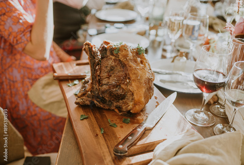 Close up of a roast beef or lamb joint on a wooden platter with a knife on a table at a party 