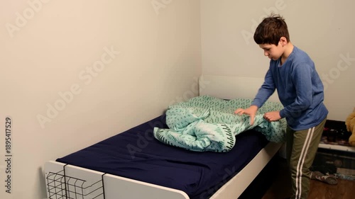 Focused boy stretches across the mattress, smoothing a green duvet in a wide side view with ample copy space. Teaching kids self reliance builds healthy routines and confidence at home.