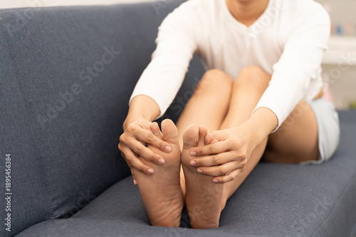 Close up of Asian woman sitting on sofa holding feet, suffering from numbness and tingling in toes, foot pain, nerve problem and health issue at home. numbness, foot, feet, toes, tingling, pain.