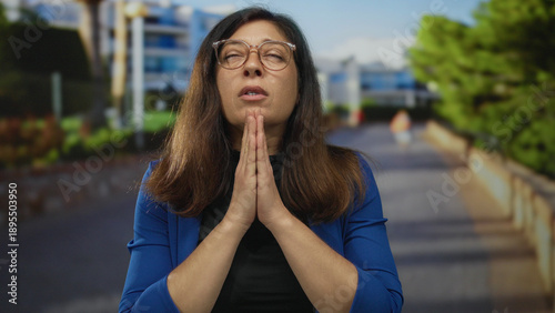 Φωτογραφία Middle age hispanic woman wearing glasses with palms pressed together in prayer gesture on street; serenity
