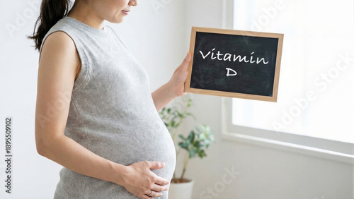 Pregnant woman holding chalkboard with vitamin D text, expecting mother in striped dress standing by window, emphasis on prenatal health nutrition balance, maternity wellness lifestyle concept