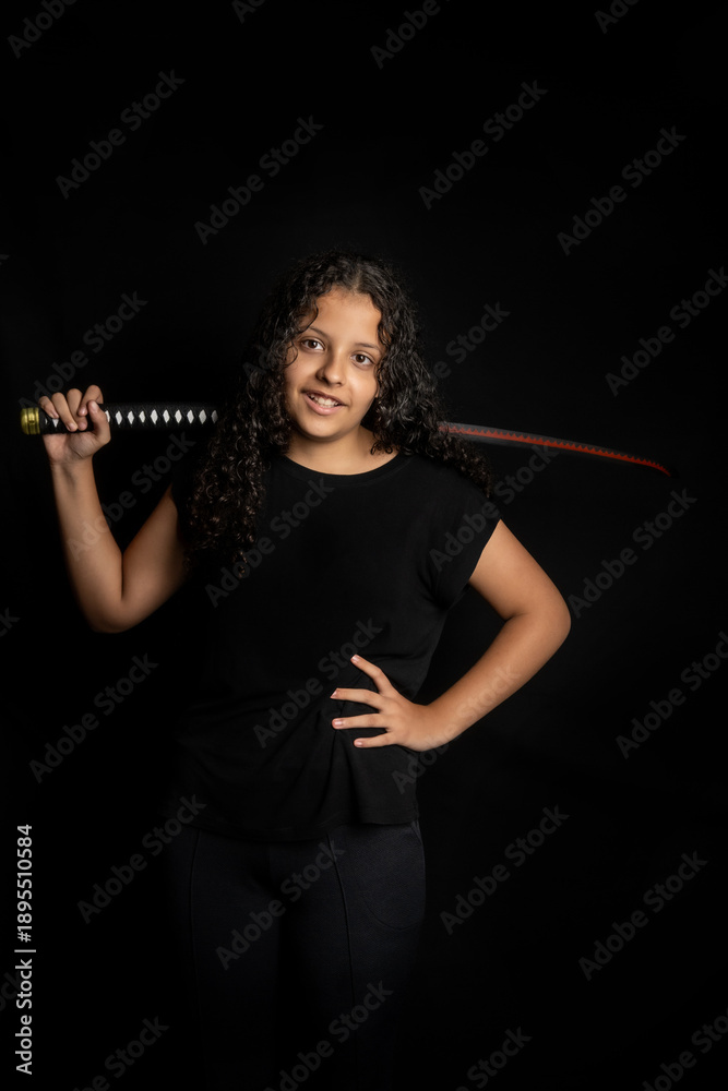 Fototapeta premium Brazilian teenager, a beautiful young Brazilian woman with a Japanese sword, low key, black background, selective focus.