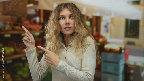 Quadro em tela Scene of a woman raising her finger while pointing to items in a busy market where a blonde young newcomer looked surprised near the fruit stall to inspect the produce