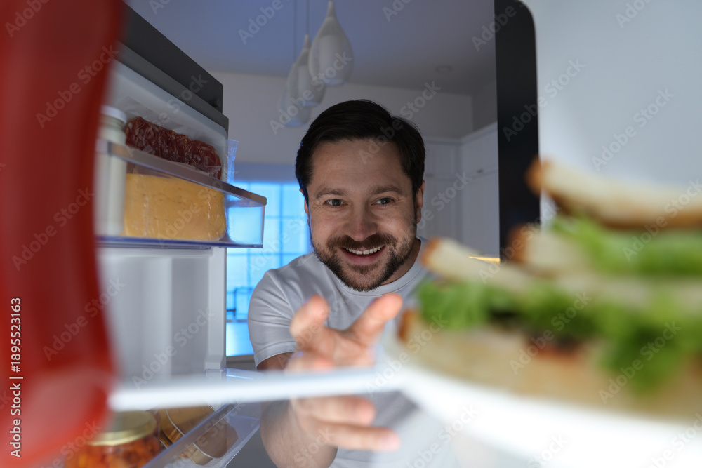 Naklejka premium Man looking into open refrigerator in kitchen, view from inside