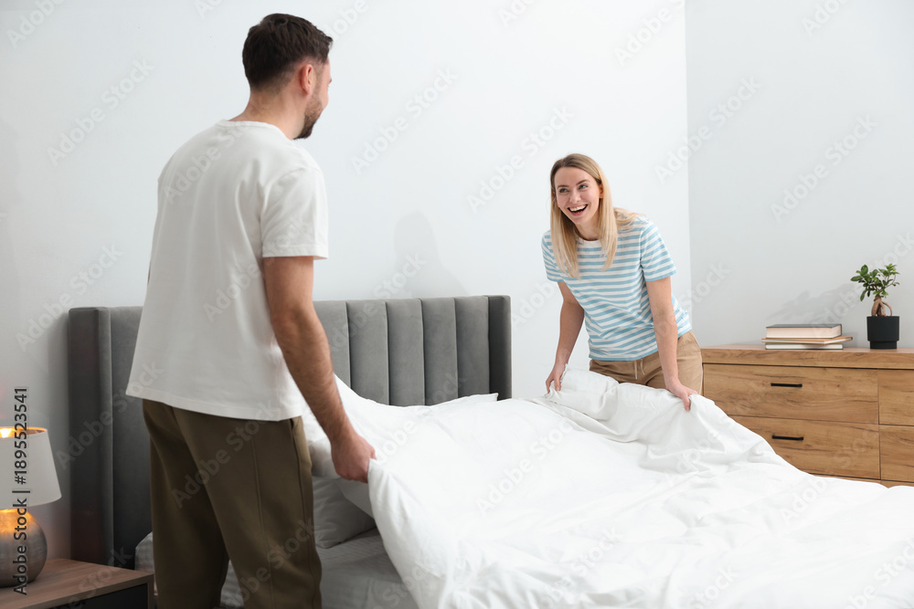 Fototapeta premium Couple changing bed linens in bedroom. Domestic chores