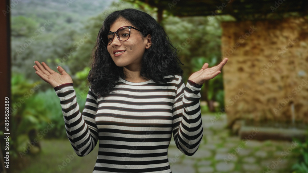 Naklejka premium Woman rubbing eyes and shrugging hands in black and white striped top near stone building on a green path; playful confusion.