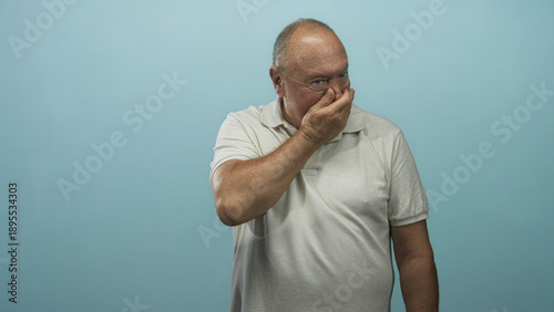 Quadro su tela Man pinching nose and covering mouth with hand while squinting in a studio setting against a blue backdrop; disgust