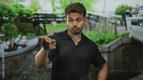 Fotografie Man points index finger toward a canal boat on a street in amsterdam, visible forearm and pointed gesture; warning confrontation
