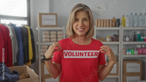 Schilderij op canvas Woman holds volunteer shirt label with bare hands in building donation room filled with boxes and shelves; charity support