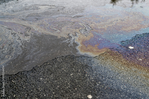 Iridescent oil and fuel streaks across puddle on asphalt.