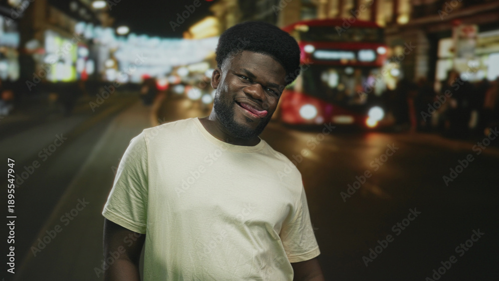 Fototapeta premium Man sticks tongue out and smiles on a busy neon lit city street with a double decker bus at night; playful urban confidence.