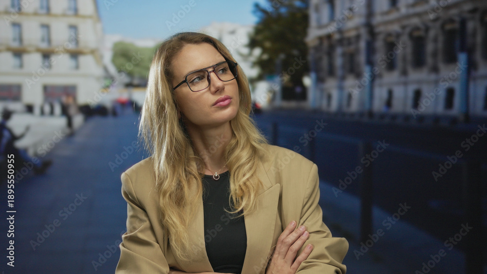 Fototapeta premium Woman standing on city street with arms crossed looking disgusted outdoor in an urban setting, featuring a young, blonde, caucasian woman in a blazer.